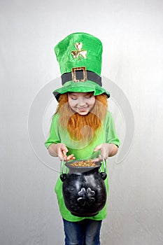 Smiling cute girl with red beard in green clothes, leprechaun\'s hat looking at cast iron leprechaun pot with gold