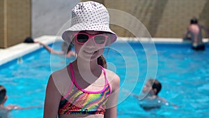 Smiling cute little girl on background of swimming pool on sunny day. Summer camp vacation concept