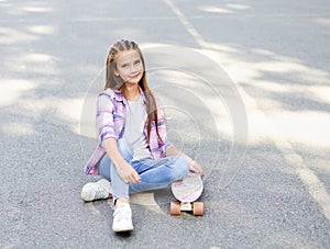 Smiling cute little girl child sitting with a skateboard. Preteen with penny board outdoors