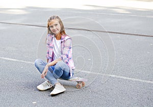 Smiling cute little girl child sitting with a skateboard. Preteen with penny board outdoors