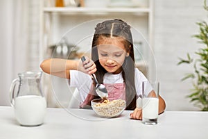 Cute little girl eating breakfast: cereal with the milk