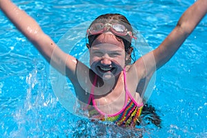 Smiling cute little girl in goggles in swimming pool on sunny summer day