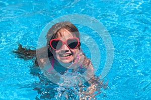 Smiling cute little girl in heart shaped sunglasses in swimming pool on sunny day