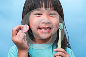Smiling cute little girl holding toothbrush and sweets isolated on blue background. Kid training oral hygiene and Unhealth eat. photo