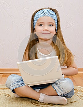 Cute little girl with a laptop at home on the floor
