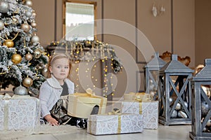 Smiling cute little girl opening a Christmas gift, the background Christmas tree