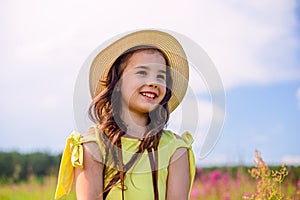 A smiling cute girl, in a straw hat , stands in nature in the summer, against the background of a blue sky, looks away