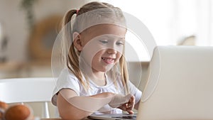 Smiling little girl using laptop close up, looking at screen