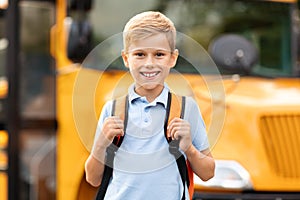 Smiling cute preteen boy posing near yellow school bus outdoors