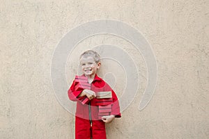 Smiling cute toddler boy in a red overalls uniform holds many small boxes