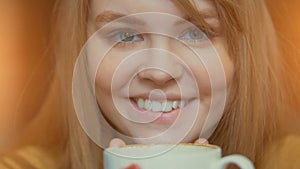 Smiling cute woman holding cup of hot coffee in hands. Inhaling aroma and relaxing