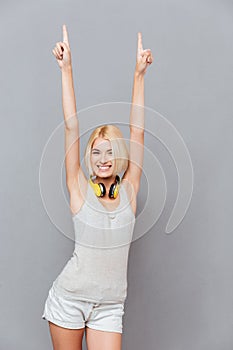 Smiling cute young woman pointing up with both hands