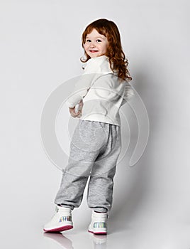 Smiling cutie little toddler girl in sportswear turning to camera from back