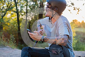 smiling cyclist, with tattoos, sits on a bicycle, with a smartphone in his hand