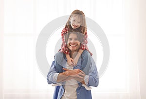 Smiling dad carrying his cheerful little daughter on shoulders