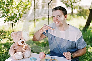 Smiling dad drinking tea from a toy cup at a table in the garden