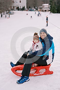 Smiling dad with a little girl in his arms sits on a sled on a snowy plain