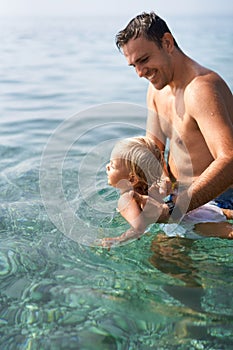 Smiling dad teaches little daughter to swim holding her hands under armpits