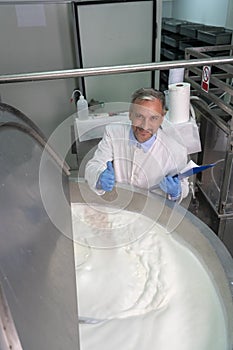 Smiling Dairy Plant Food Engineer Giving Thumbs Up Beside Stainless Steel Milk Pasteurizer Tank