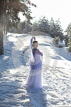 Vertical portrait against the background of the winter landscape of a cute brunette in a long white dress and a light purple