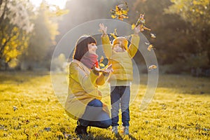 Smiling daughter throwing autumn leaves and having fun on a walk with her pretty loving mother