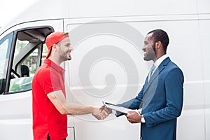 smiling delivery man and african american businessman shaking hands