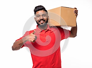 Smiling delivery indian man in blue uniform carrying packages while gesturing thumb up sign isolated on white background