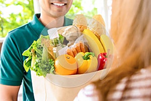 Smiling delivery man giving grocery bag to woman customer at home