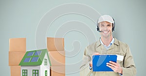 Smiling delivery man holding clipboard by house and parcels