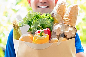 Smiling delivery man holding a grocery bag ready to deliver to the customer