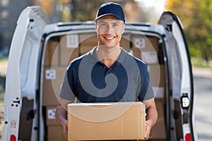 Smiling delivery man standing in front of his van holding a package photo