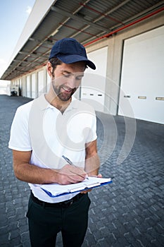 Smiling delivery man writing on clipboard