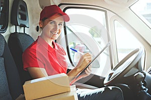 smiling delivery person in red uniform sitting in van and writing documents