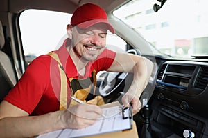 Smiling delivery service worker fill in necessary documents after shipping