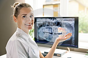 smiling dentist with dental typodont, teeth model in hand in clinics office