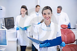 Smiling dentist holding file at dental clinic