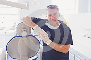 Smiling dentist leaning against dentists chair photo