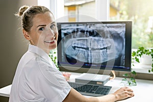 smiling dentist working with dental x-ray image on computer in clinics office