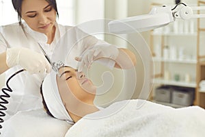 Smiling dermatologist making procedure of facial oxygen therapy for young woman