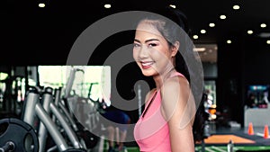 Smiling and determined youthful Asian female athlete looking at camera while putting arms crossed and standing at gym