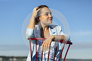 Smiling digital nomad, female business entrepreneur sits in chair in water, blue sky is on