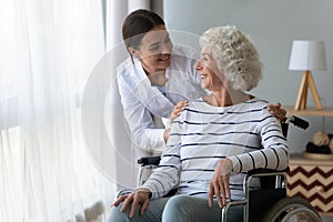 Smiling disabled elderly woman in wheelchair talking with caring nurse