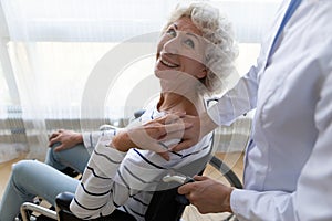 Smiling disabled retired female older patient feeling thankful to physiotherapist.