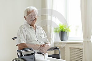 Smiling disabled senior man in a wheelchair alone at home