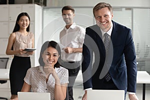 Smiling diverse business leaders posing with computers and team people