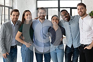 Smiling diverse business people hugging, standing in modern office