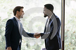 Smiling diverse businessmen handshake closing deal in office