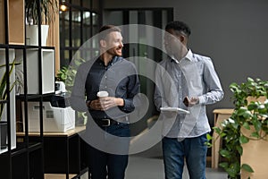 Smiling diverse colleagues talking, walking in modern office