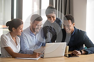 Smiling diverse employees laugh cooperating at laptop in office