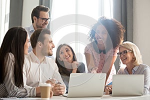 Smiling diverse employees laugh working together at laptop in office